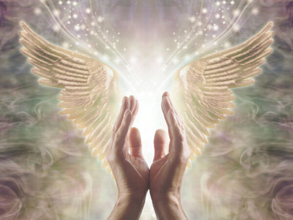 Male hands reaching up into a beautiful pair of golden Angel wings with white light and sparkles flowing  between, against a warm ethereal energy formation background